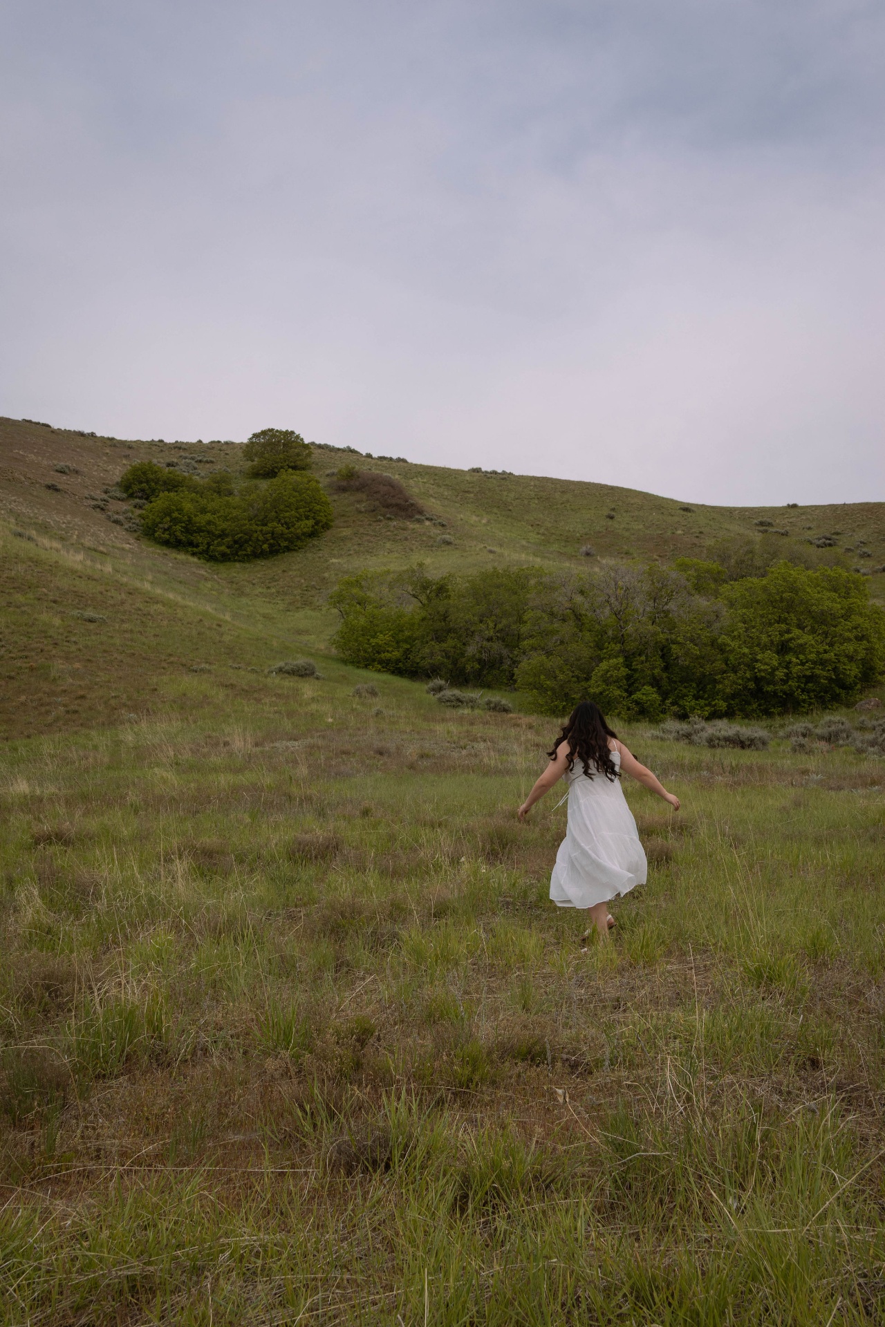 Woman in a white dress walking through a green hillside meadow