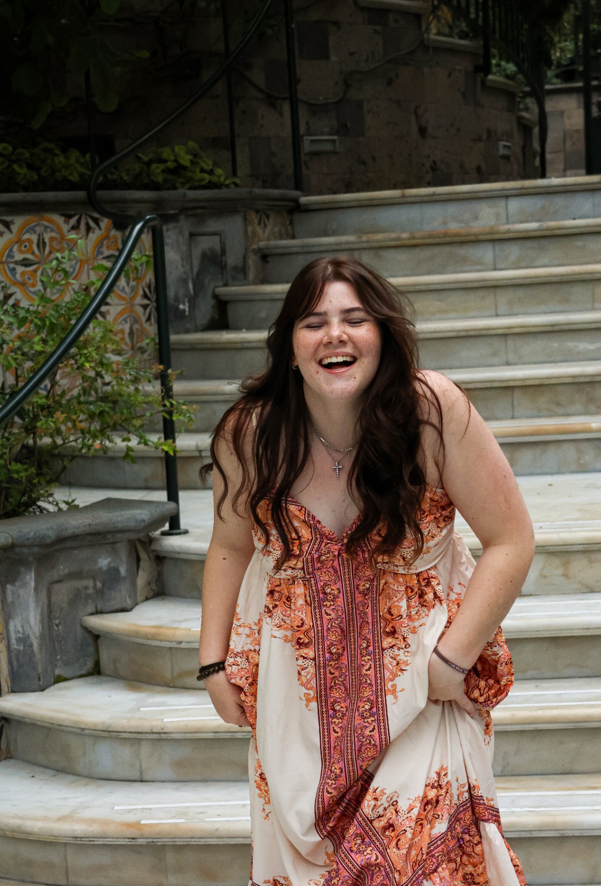 Young woman in a paisley dress laughing freely on stone steps